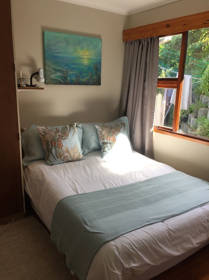 A bedroom with a bed, a painting, a window with curtains, and a shelf with a lamp.