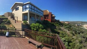 Une propriété située sur la côte, dotée d’une terrasse en bois, d’un escalier menant à une maison et offrant une vue sur l’océan.