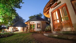 A bungalow-style hotel with a thatched roof, a well-lit entrance, and a sign indicating the name 'JO30'. - Ivory Wilderness River Rock Lodge (Bushbuckridge)