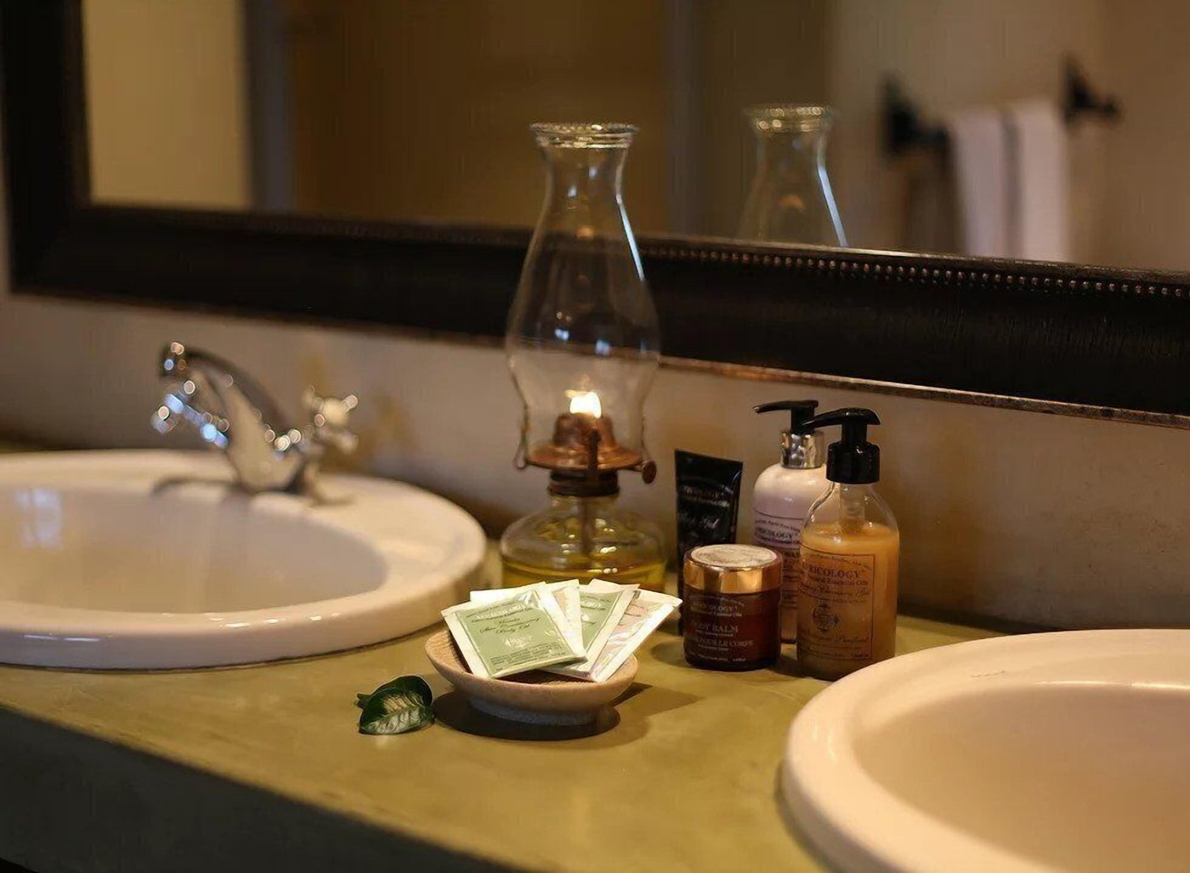 Un lavabo de salle de bain avec des articles de toilette, un miroir et un joli flacon en verre décoratif avec une lumière.