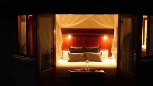 A dimly lit room with a bed, a bedside table, and a window with curtains. - Ivory Wilderness River Rock Lodge (Bushbuckridge)