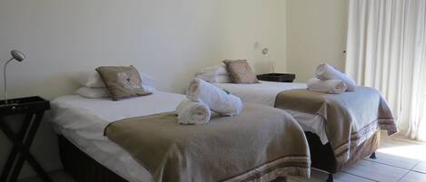 Habitación de hotel con dos camas, cada una con una toalla enrollada y una manta marrón. Se observa un mesita de noche con una lámpara y una pequeña bandeja negra.