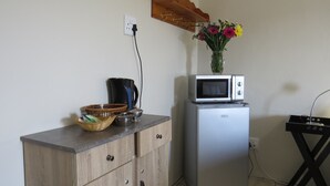 A kitchenette with a microwave, a coffee maker, a basket, and a vase with flowers.