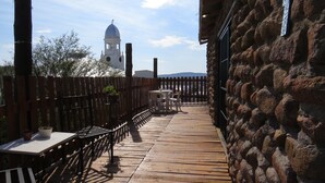 A wooden deck with tables and chairs, a stone wall, and a view of a white building with a dome and bell tower.