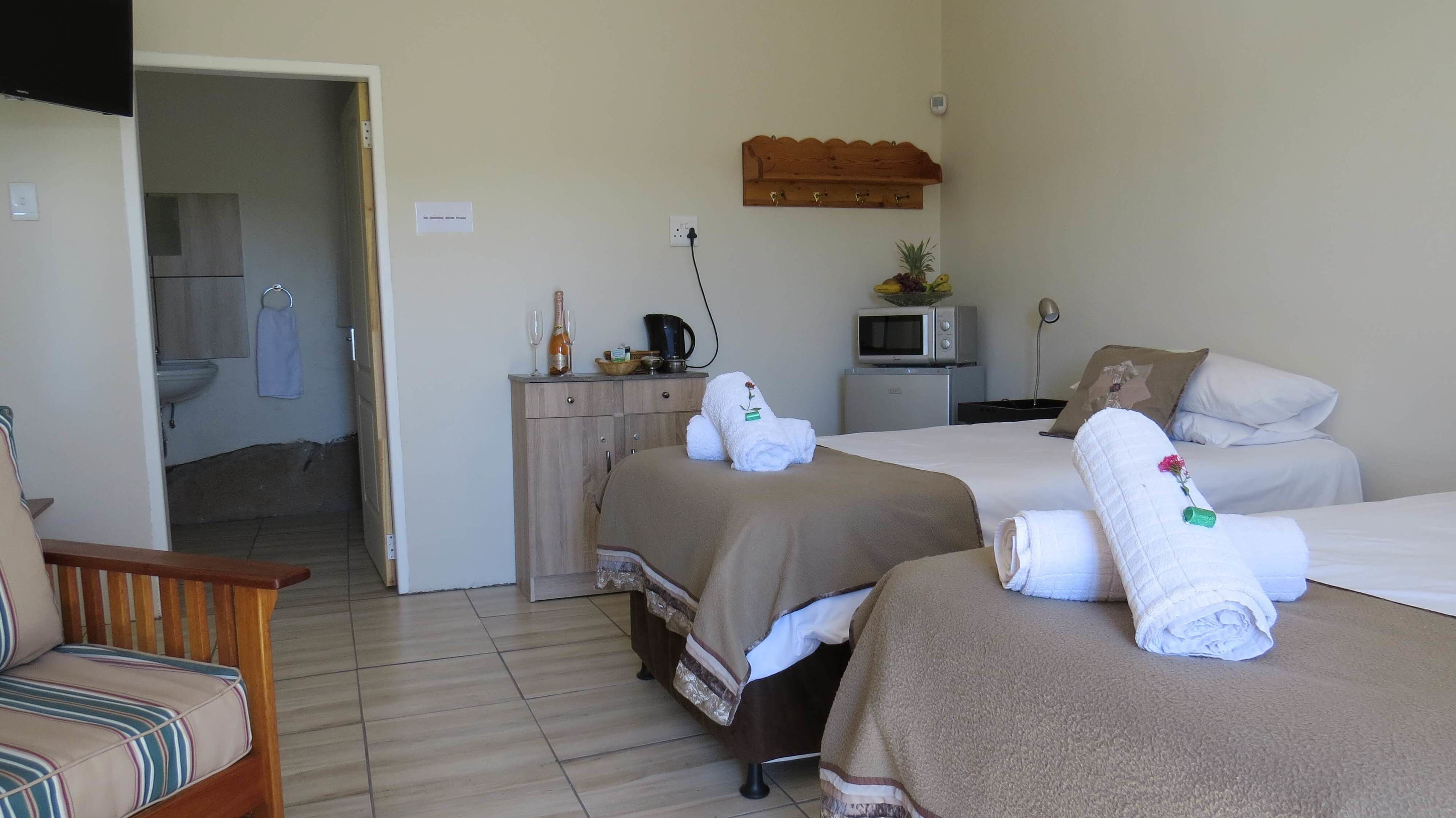 A hotel room with two beds, a desk, a microwave, a TV, and a bathroom visible through an open door.