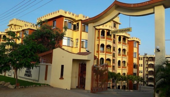 A hotel named "Sunset Paradise" with a distinctive architectural style, featuring multiple balconies and a large entrance gate.