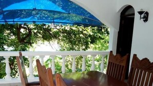 A covered outdoor dining area with a wooden table and chairs, surrounded by a white railing, and a blue umbrella providing shade. - Fastcare Luxury Apartments/Villas (Mtwapa)