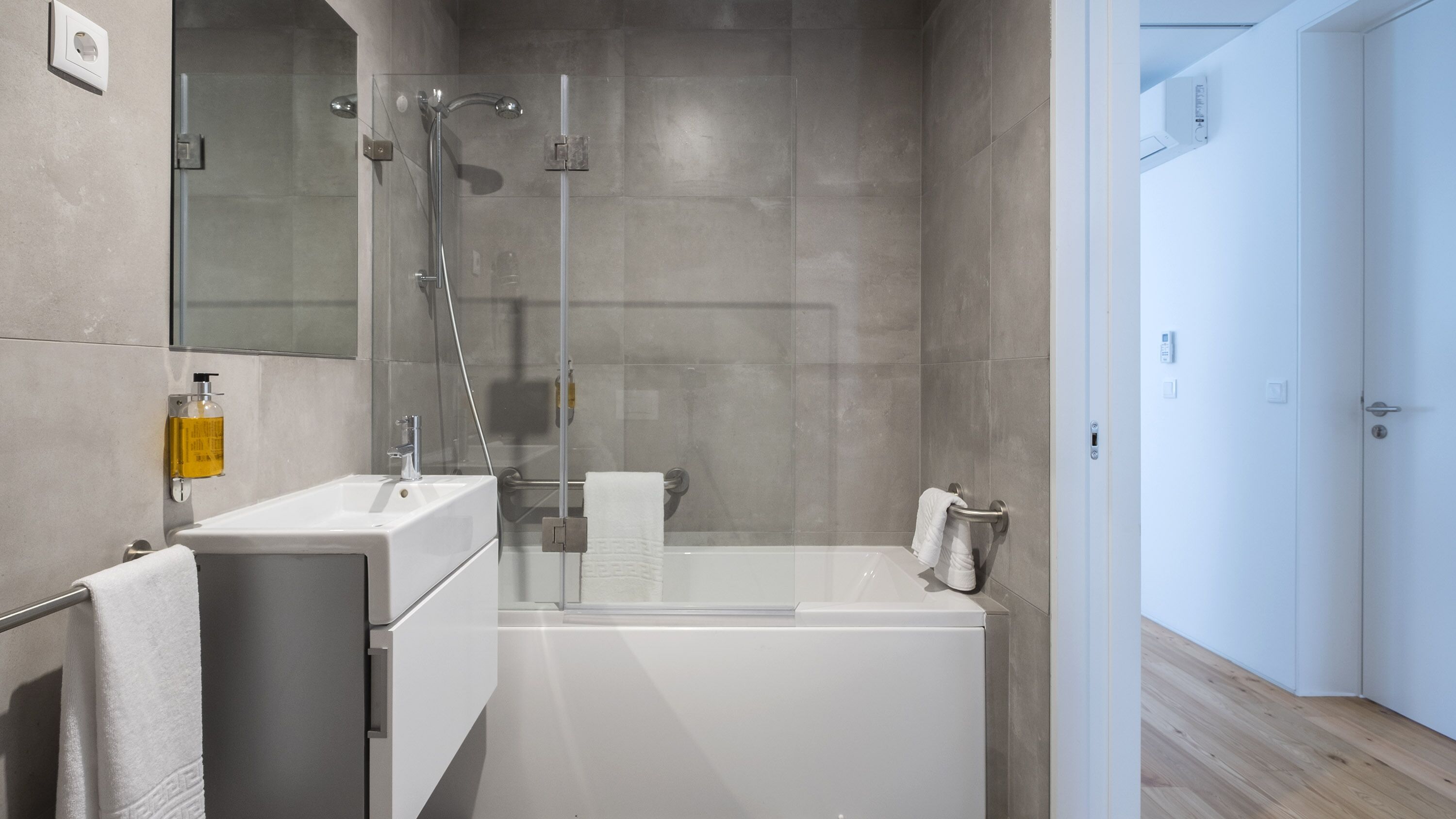 A modern bathroom with a glass-enclosed shower, a white sink, and a towel rack.