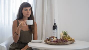 A person sitting at a round table with a white plate, a bottle of wine, a pineapple, and a bowl of grapes.