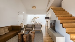A modern living room with a wooden staircase, a sofa, a coffee table, and a dining area. - Aqua - Pópulo Eco Village (Ponta Delgada)