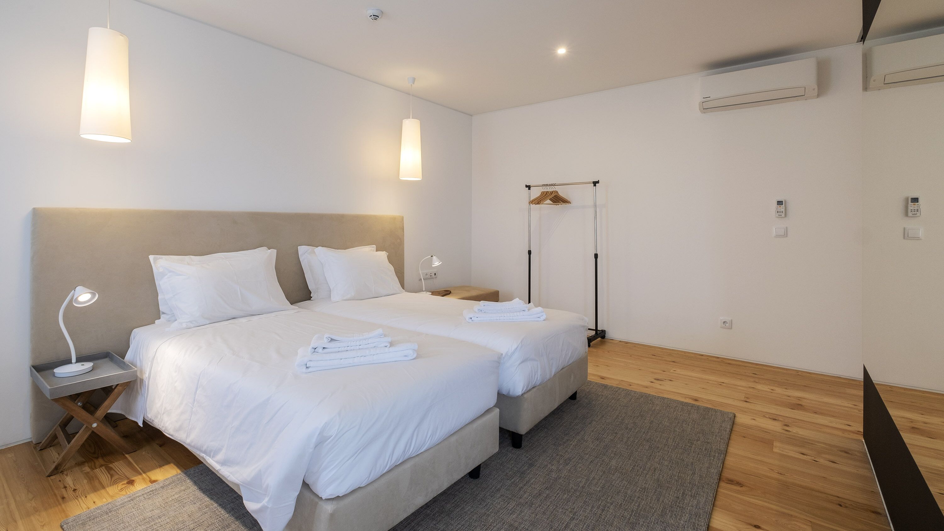 A hotel room with two beds, a bedside table with a lamp, a standing lamp, a shower area, and a small bedside table with a phone.
