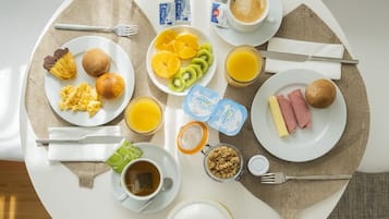 Una mesa de desayuno con diversos alimentos, como huevos, tostadas, fruta y café.