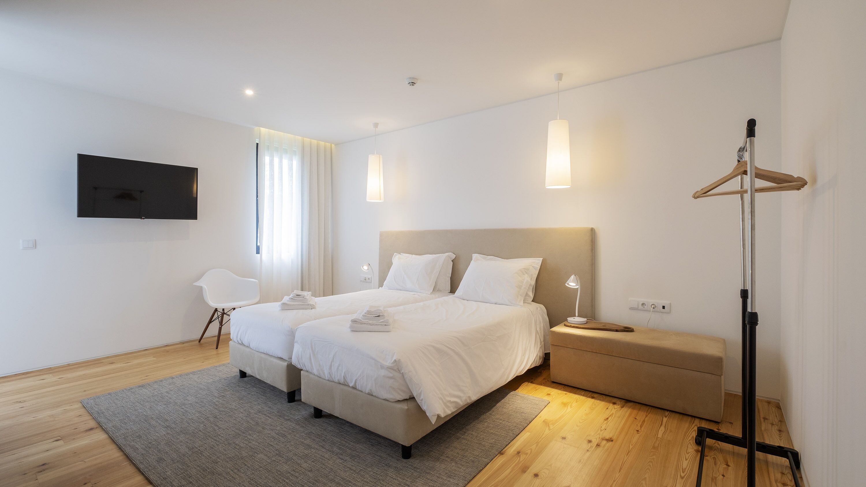 Una habitación de hotel moderna con una cama grande, mesitas de noche, un televisor montado en la pared y un perchero.