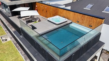 A modern rooftop pool with glass barriers, a hot tub, and outdoor seating.