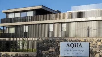 Een modern gebouw met een stenen muur en een bord waarop staat: "AQUA pueblo eco village".