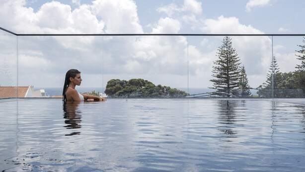 A person in a glass-enclosed infinity pool with a clear view of the ocean and trees. - Aqua - Pópulo Eco Village (Ponta Delgada)