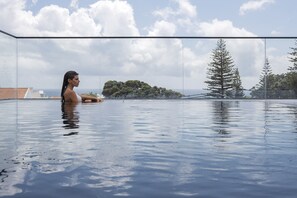 Una persona en una piscina d'hidromassatge amb vidre i vistes panoràmiques a l'oceà i als arbres.