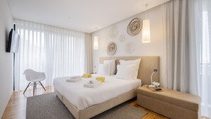 A modern hotel room with a large bed, bedside tables, a flat-screen TV, and a seating area with a sofa and a chair. - Aqua - Pópulo Eco Village (Ponta Delgada)