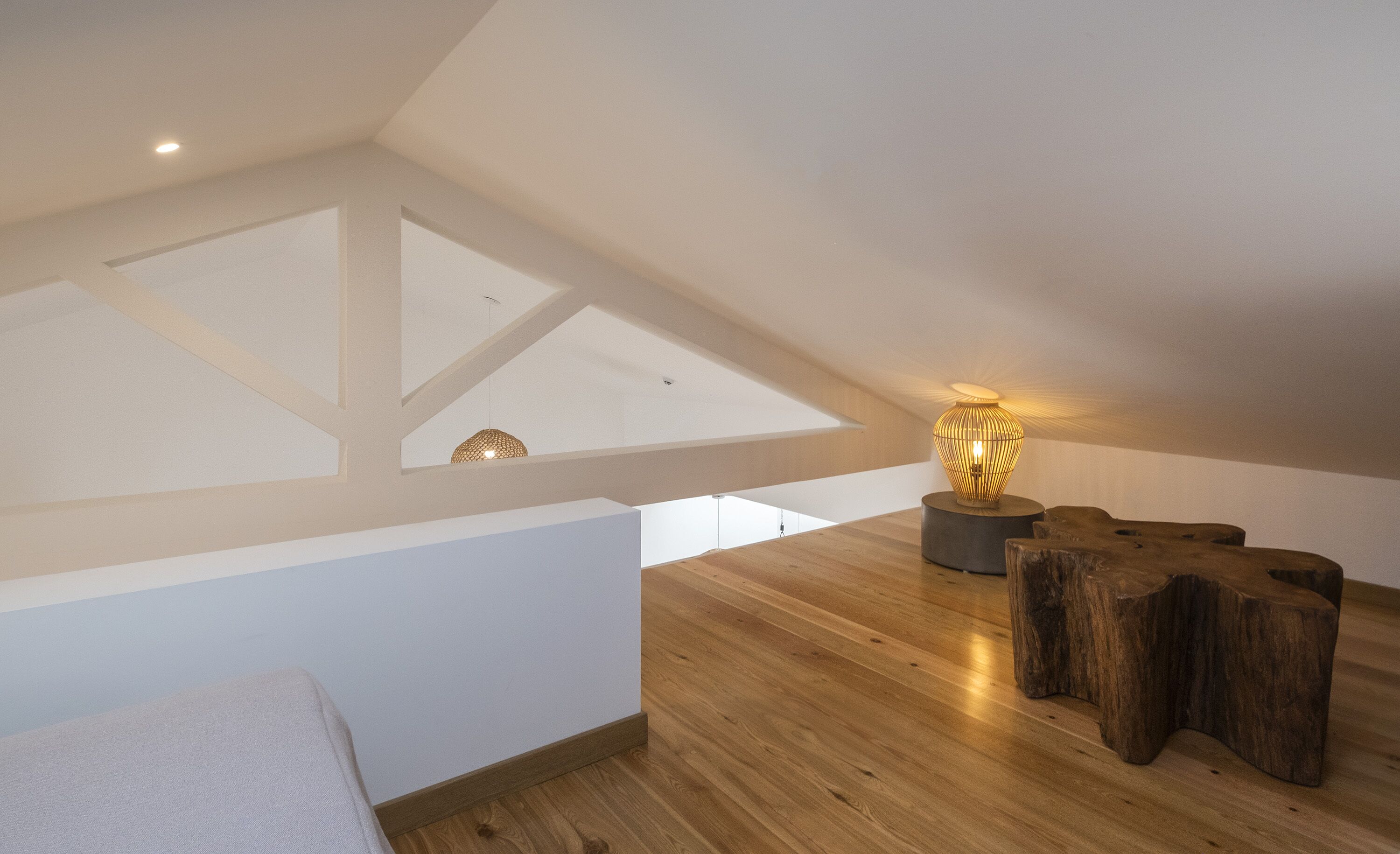 Un dormitorio tipo loft moderno con techo inclinado, suelo de madera y una lámpara original.