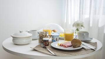 A breakfast table with a variety of food items, including a plate with eggs, ham, and a biscuit, a glass of orange juice, and a jar of jam.