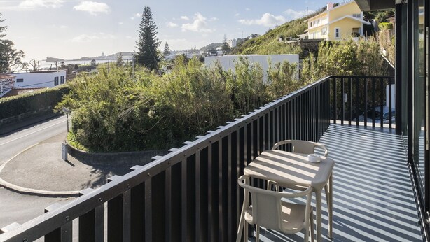 A balcony with a table and chairs, overlooking a road and greenery. - Aqua - Pópulo Eco Village (Ponta Delgada)