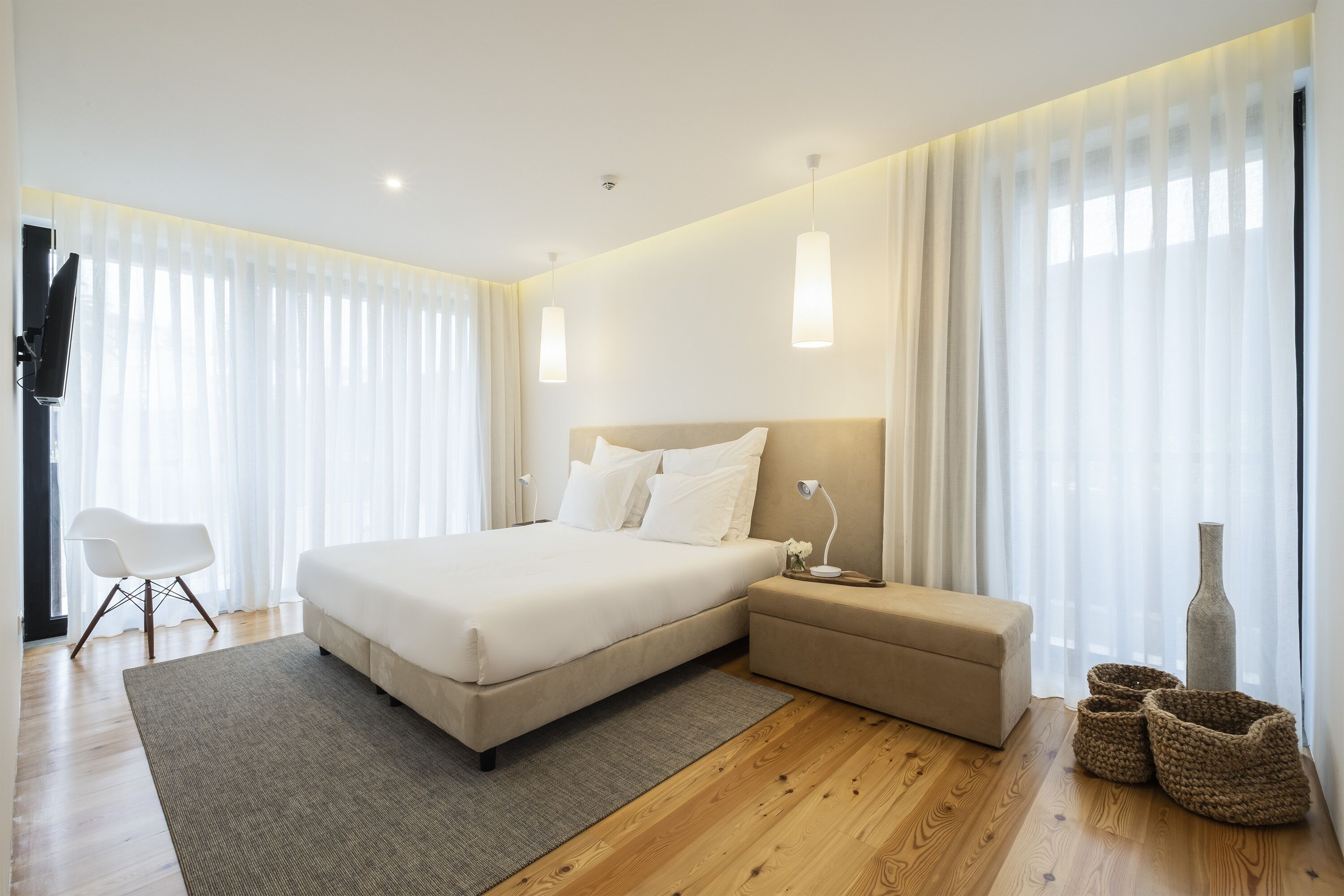 A modern bedroom with a large bed, bedside tables, a chair, and a vase.