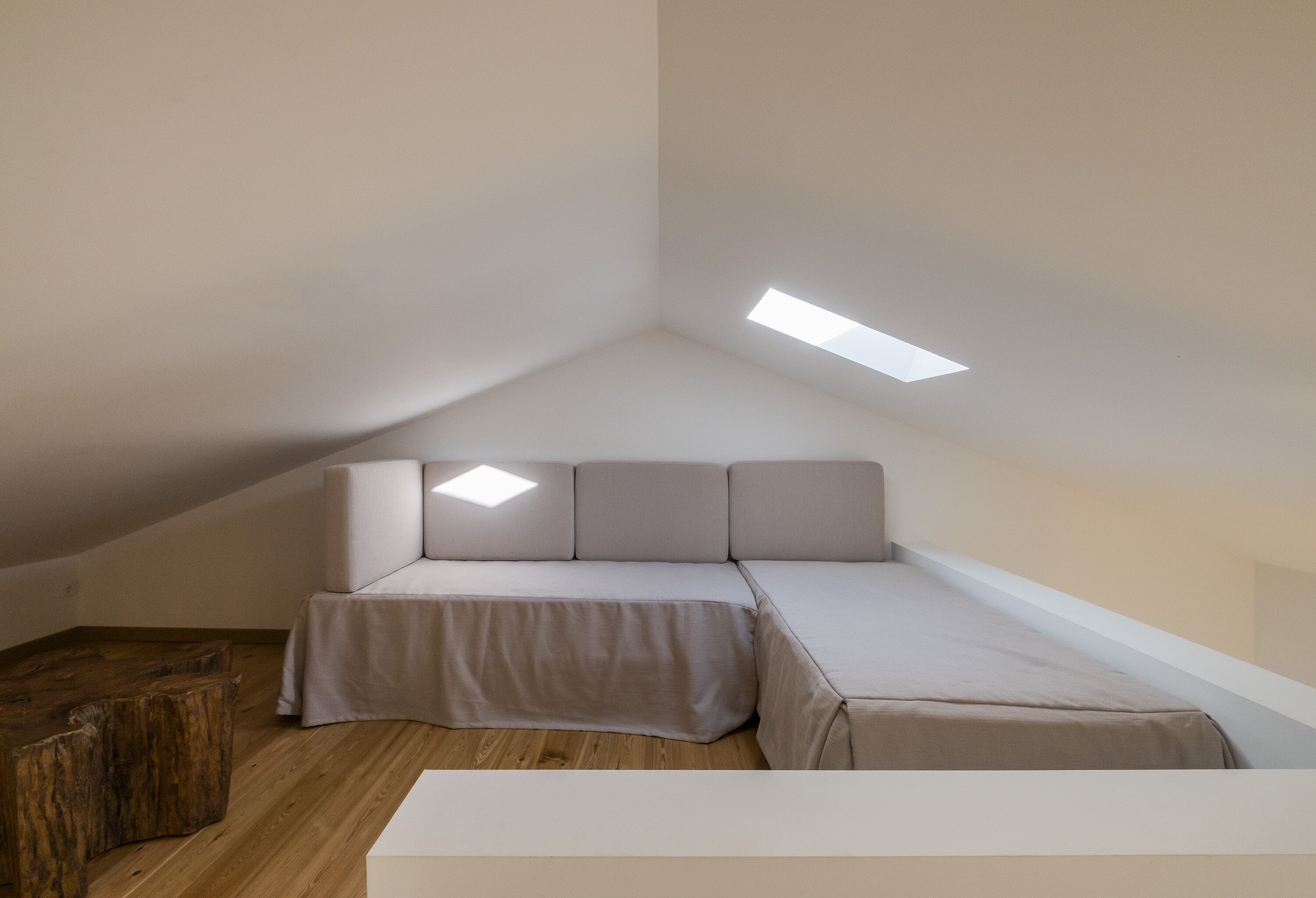 A small, modern room with a sloped ceiling, a sofa bed, a wooden coffee table, and a skylight.