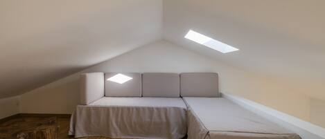 A small, modern room with a sloped ceiling, a sofa bed, a wooden coffee table, and a skylight.