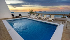Una piscina sul tetto con sedie a sdraio e vista sullo skyline cittadino al tramonto.