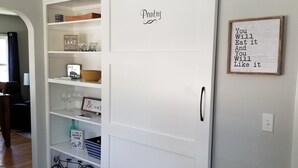 A white sliding door with the word "Pantry" on it, leading to a storage area with shelves and various items.