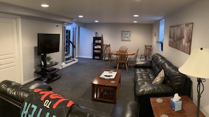 A living room with a black leather sofa, a wooden coffee table, a TV, and a dining area with a table and chairs.