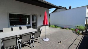 Een terras buiten met een tafel, stoelen, een rode parasol en een motorfiets in de buurt geparkeerd.