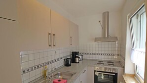Een compacte keuken met witte kasten, een roestvrijstalen afzuigkap, een gasfornuis, een koffiezetapparaat en een raam dat natuurlijk licht binnenlaat.