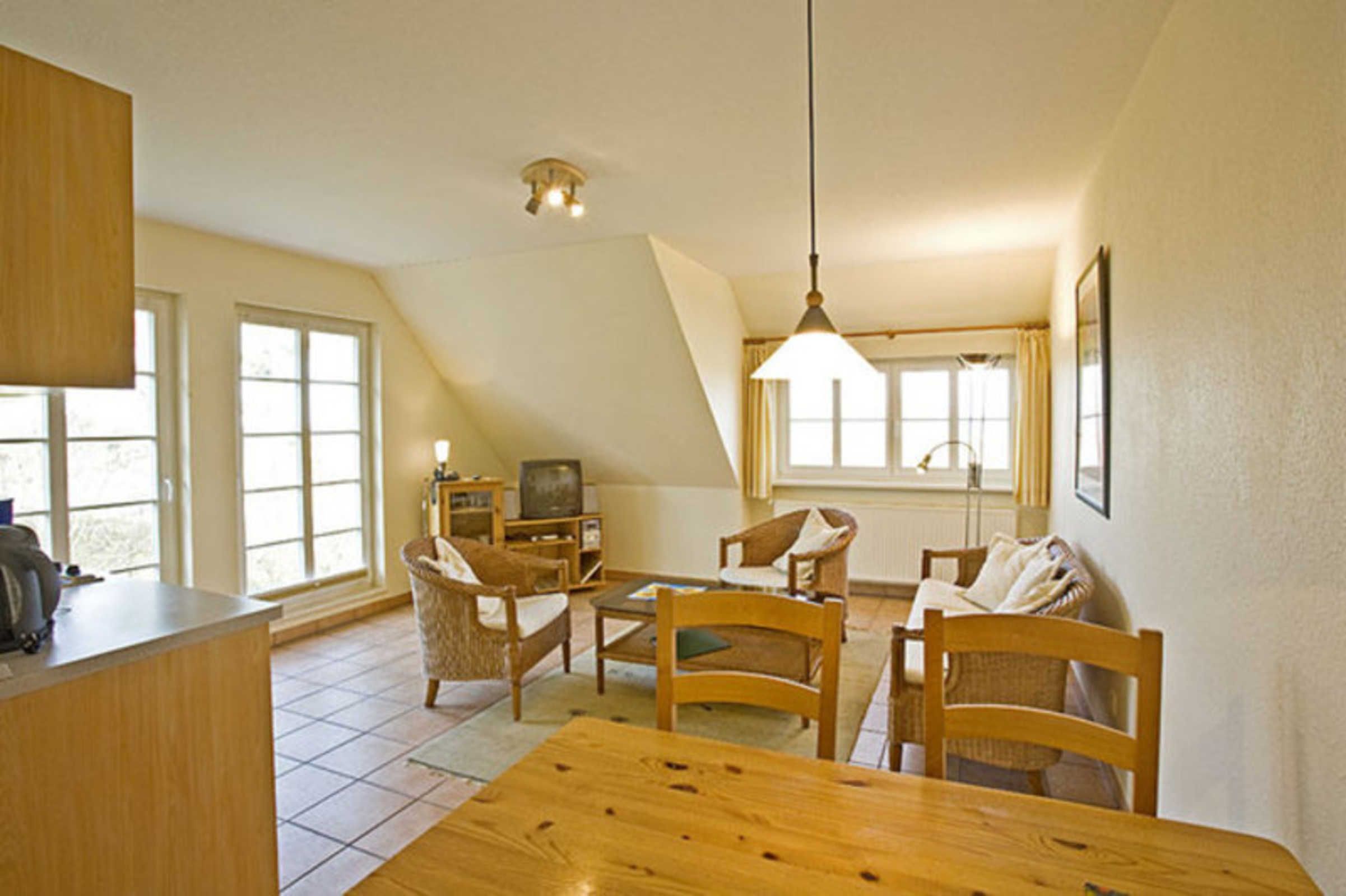 Een gezellige woonkamer met een houten eettafel, stoelen, een televisie en een keukenhoek met een aanrecht en kastjes.