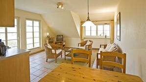 A cozy living room with a wooden dining table, chairs, a television, and a kitchen area with a counter and cabinets. - House Martha - Kurt - House Martha (Ahrenshoop)