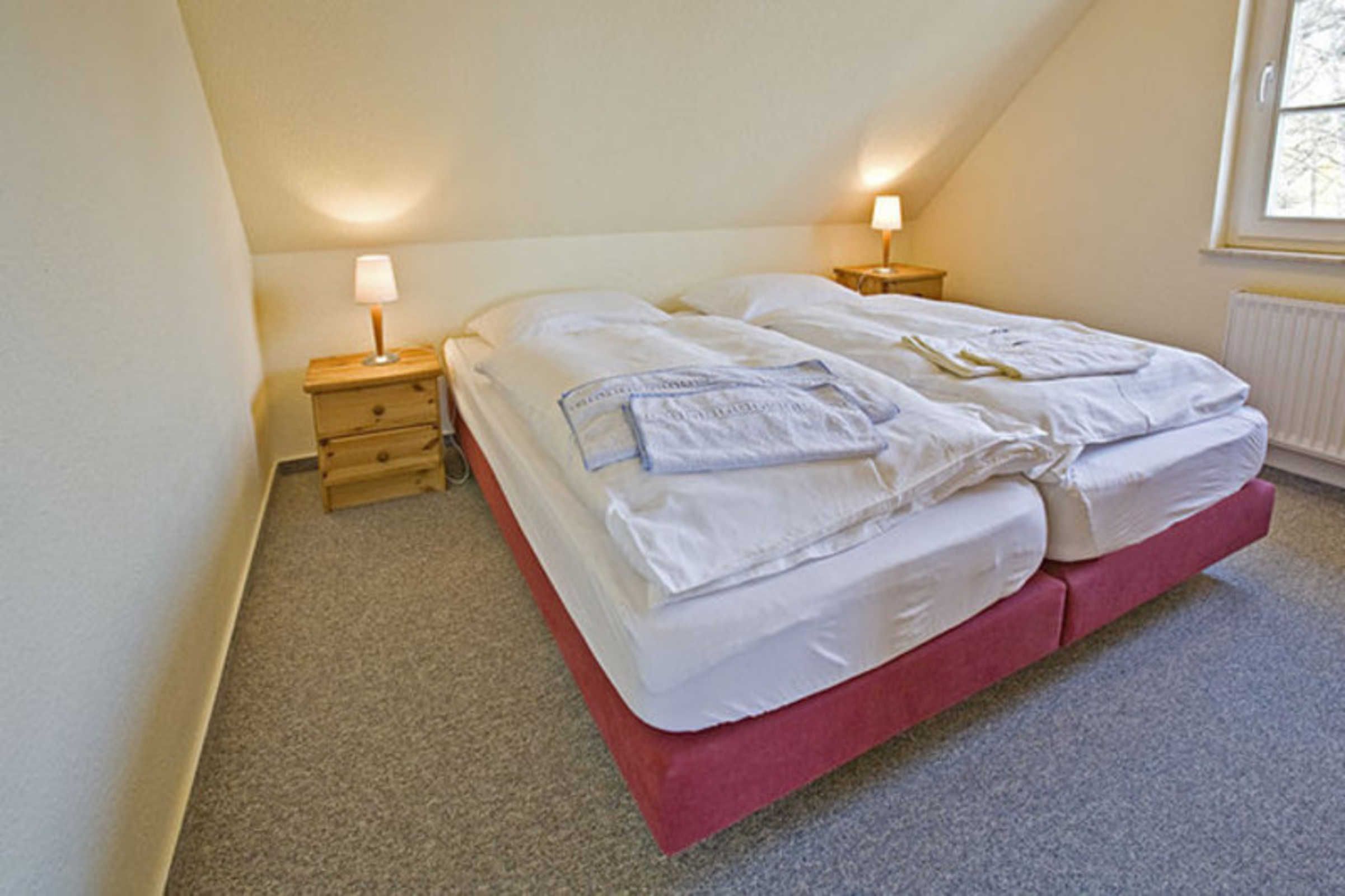 En säng för en person med en röd sängram, två sängbord med lampor och ett fönster med utsikt över träd.