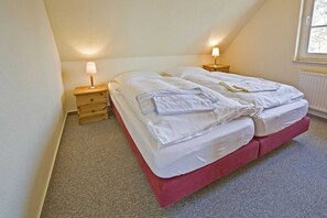 Una cama individual con base roja, dos mesitas de noche con lámparas y una ventana con vistas a árboles.