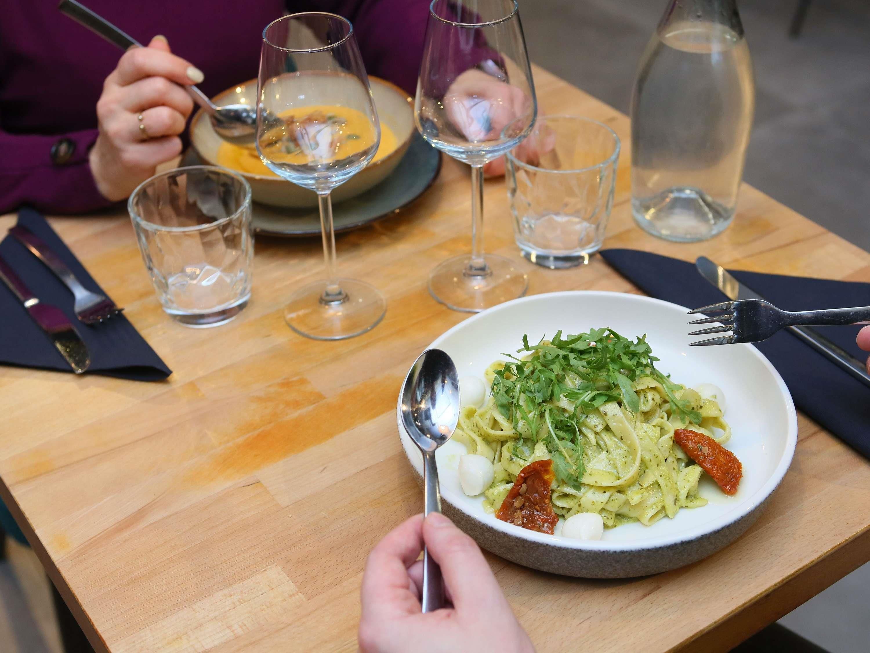 Een eettafel met een bord pasta, een vork en een lepel.