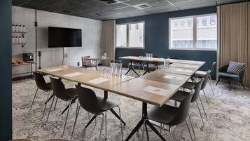 Une salle de conférence avec une longue table, des chaises noires, un téléviseur à écran plat et de grandes fenêtres dotées de rideaux.
