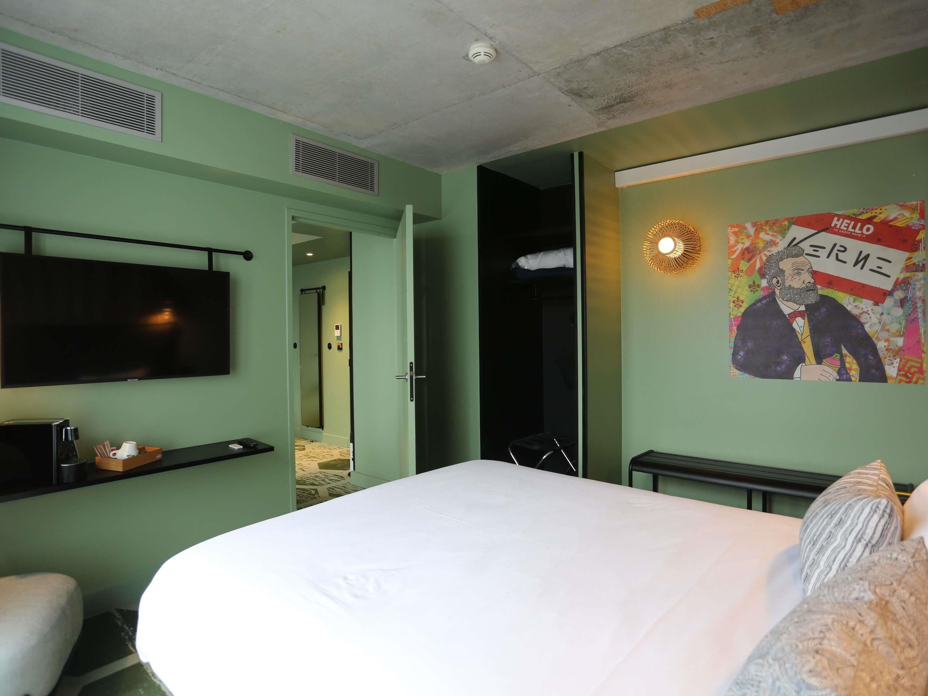 A hotel room with a bed, a flat-screen TV, a coffee machine, and a poster on the wall.