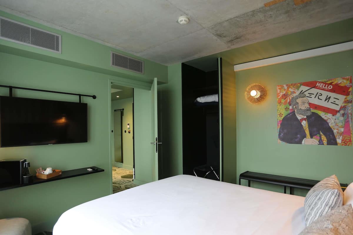 A hotel room with a bed, a flat-screen TV, a coffee machine, and a poster on the wall.