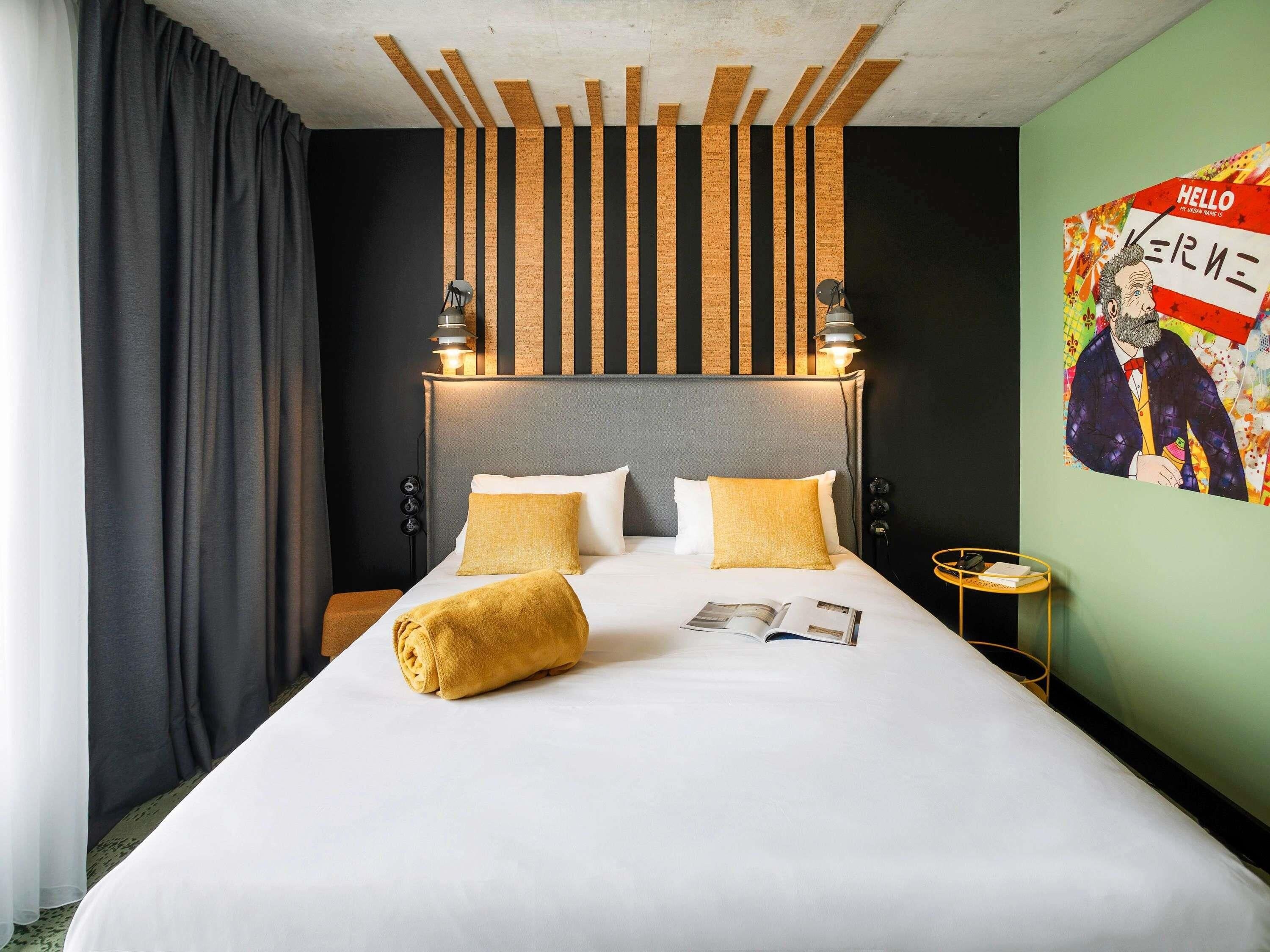 Una habitación de hotel con una cama, dos lámparas de noche, una mesita de noche, una revista y un cartel en la pared.