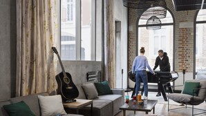Una sala de estar moderna con un sofá, una mesa de centro y una guitarra. Dos personas caminando por la habitación.