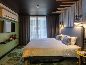 Una habitación de hotel moderna con una cama grande, un televisor de pantalla plana, una cafetera y vistas a la ciudad desde la ventana.