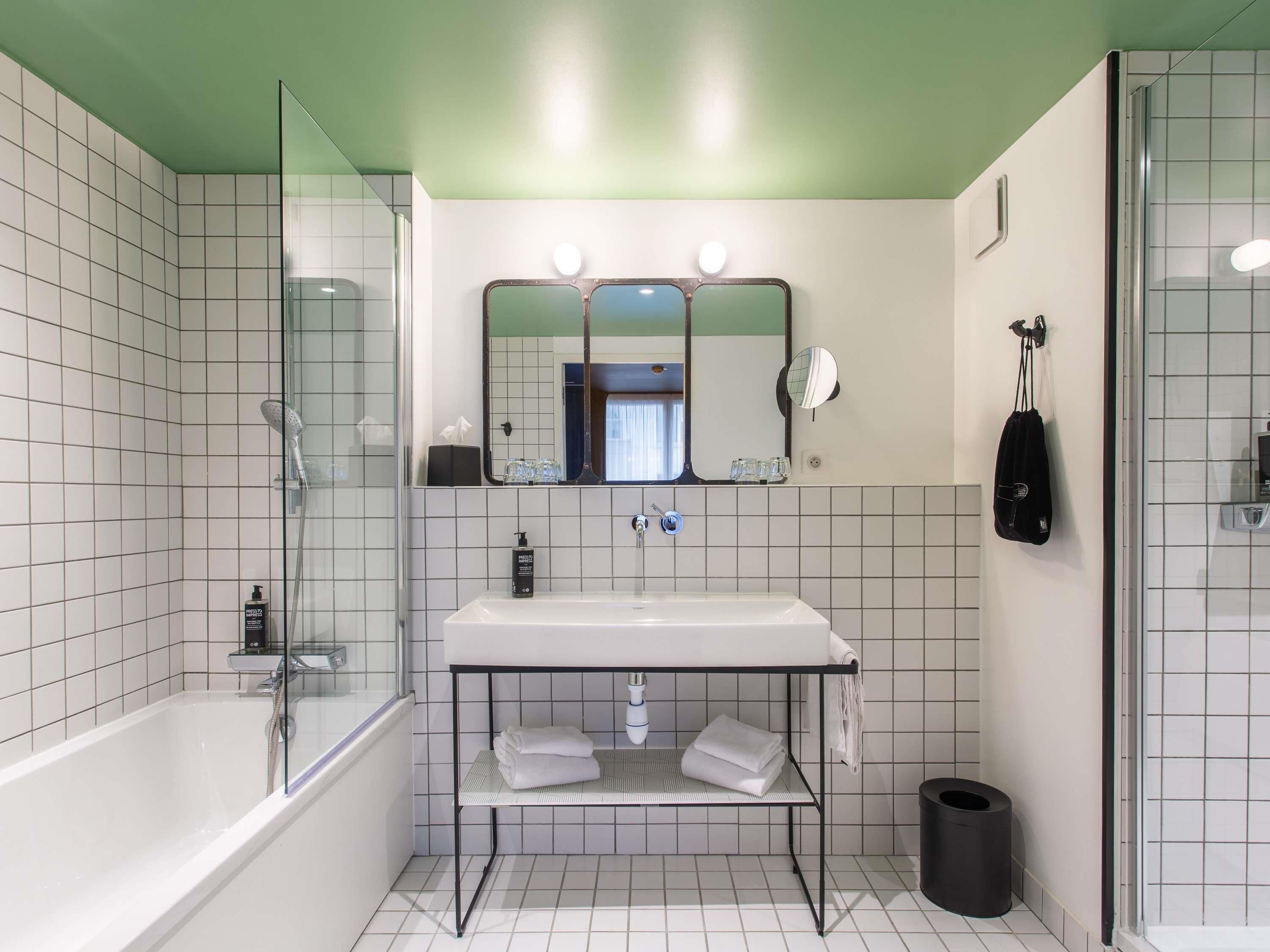 A modern bathroom with a glass-enclosed shower, a white sink with a mirror above, and a black trash bin.