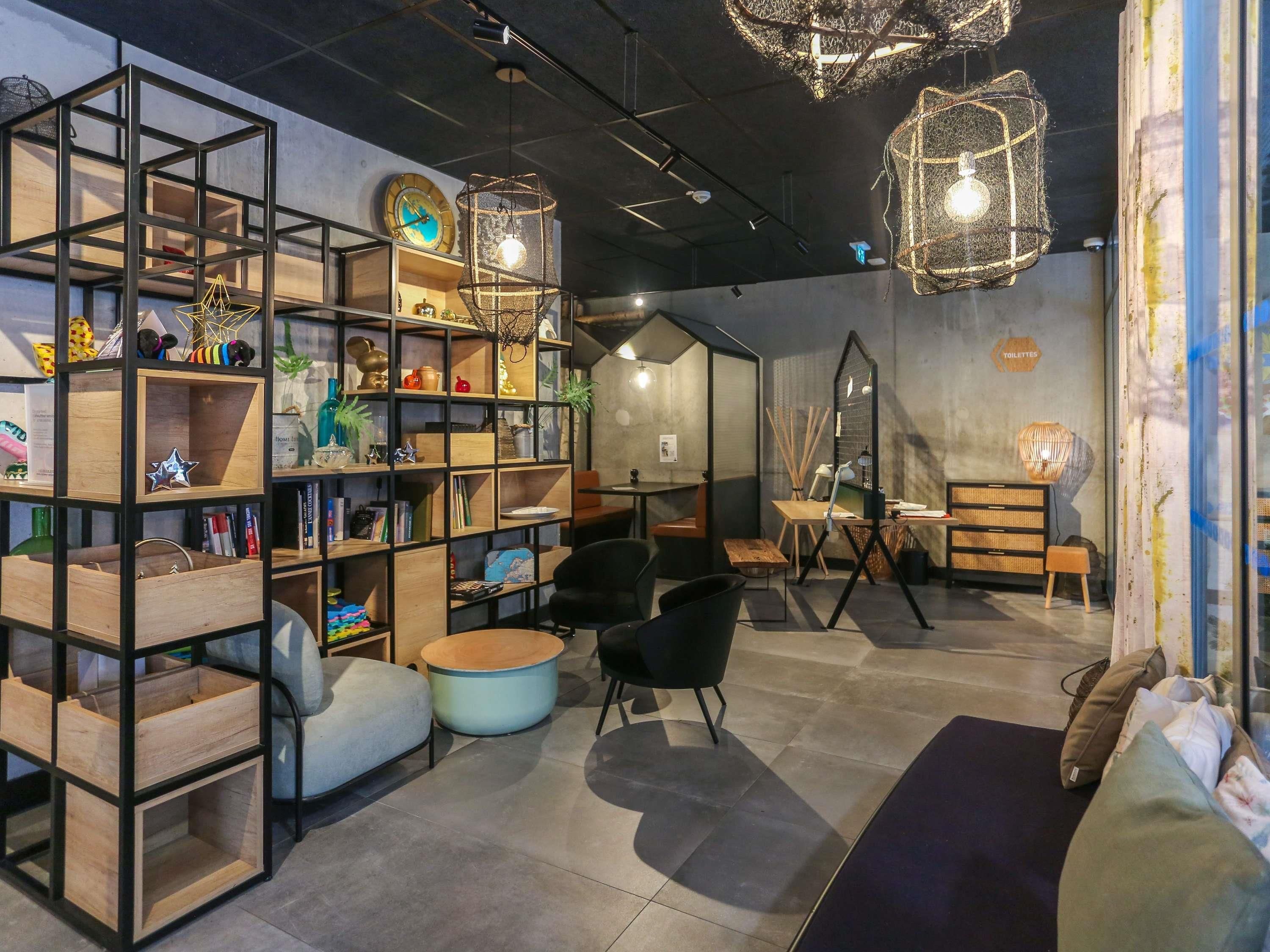 Un interior moderno con una zona de estar central, una estantería con diversos objetos y luces colgantes.