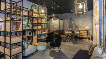 Un interior moderno con una zona de estar central, una estantería con diversos objetos y luces colgantes.