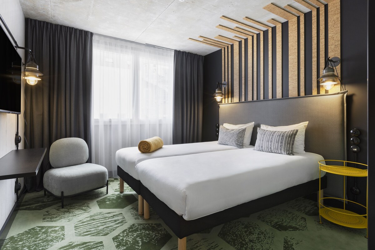 A modern hotel room with a large bed, a chair, a desk, and a TV.