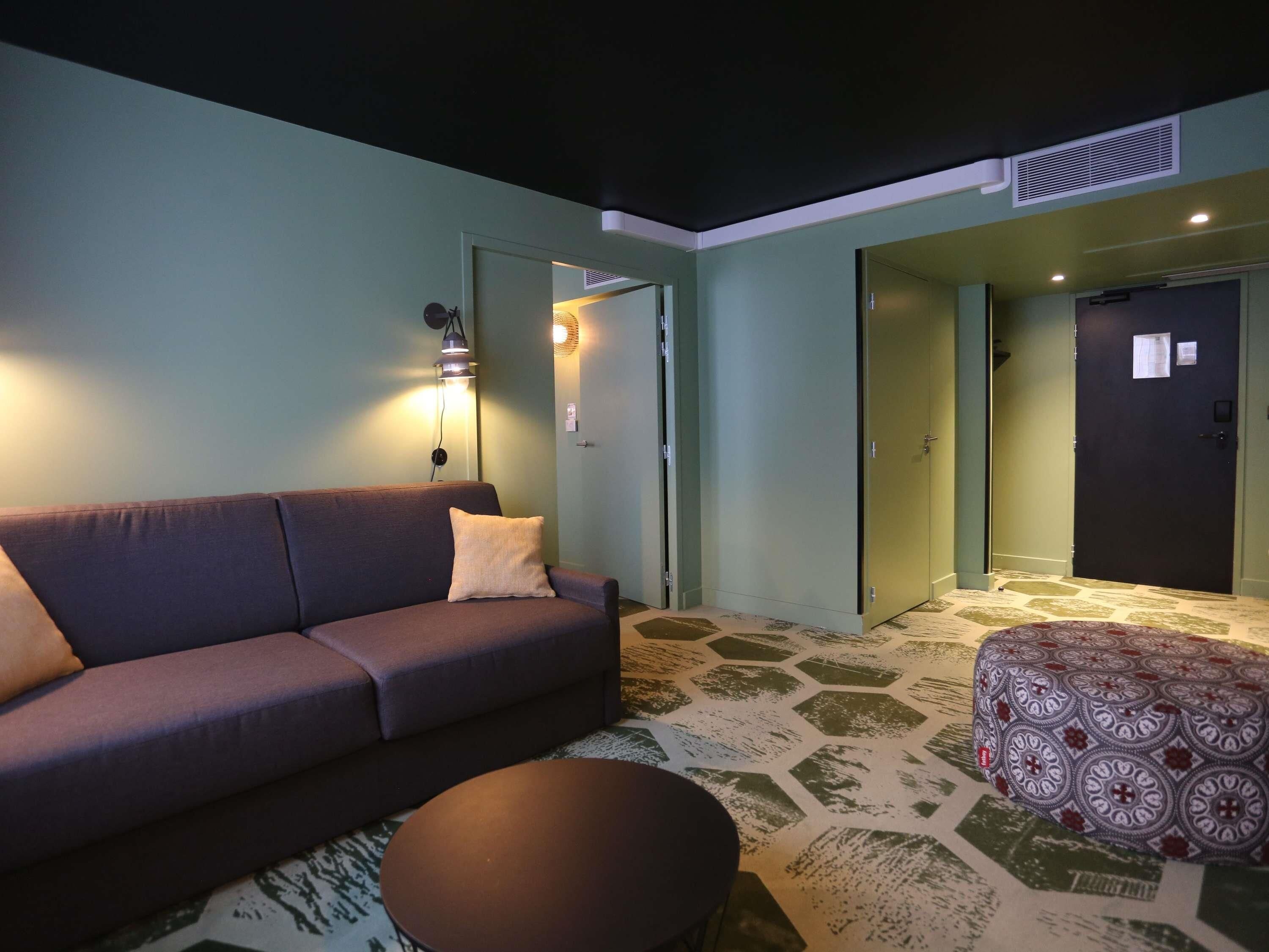 A living room with a sofa, a round coffee table, patterned carpet, and a door leading to another room.