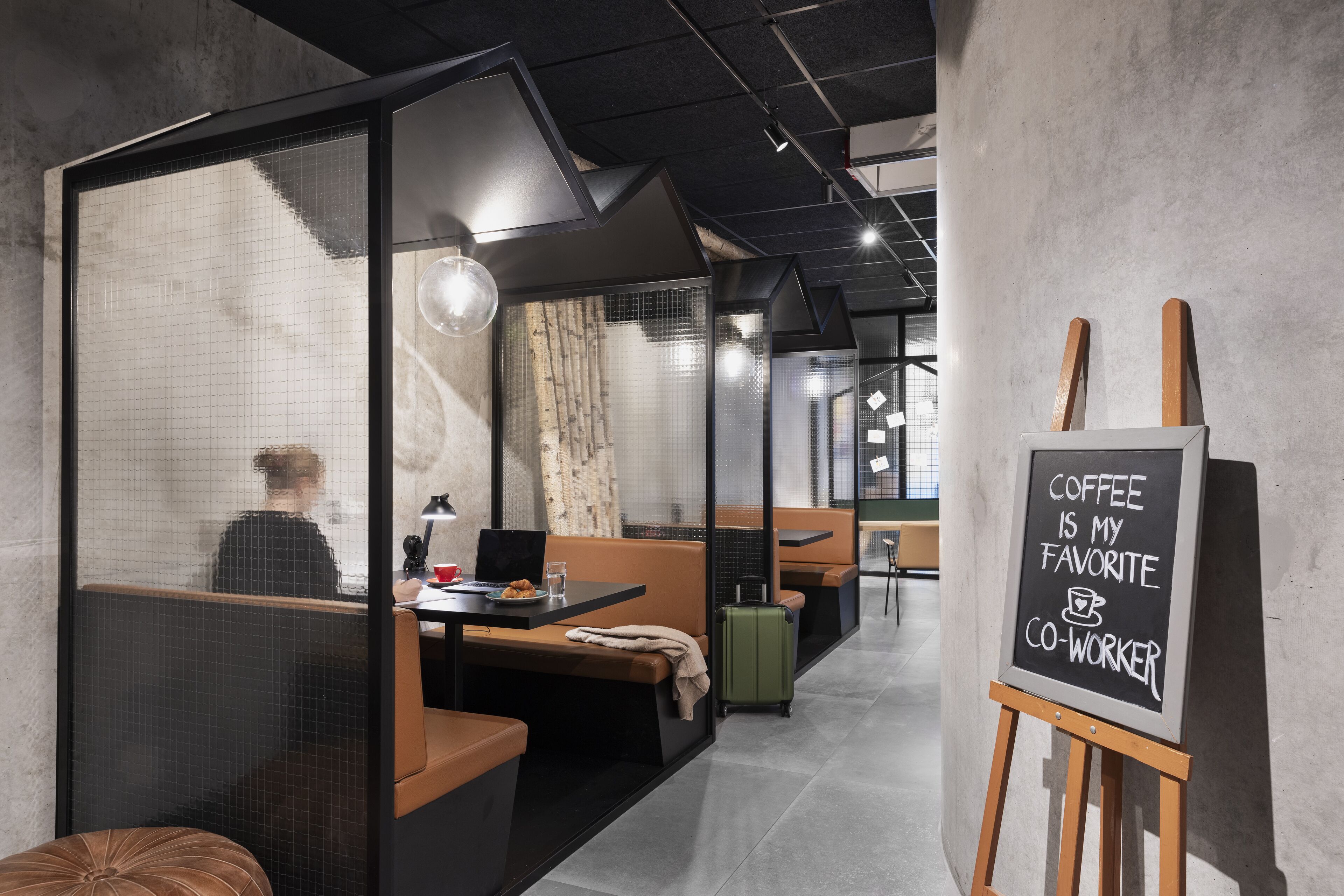 Et moderne fællesarbejdsrum med glasvægge, behagelige siddepladser og et tavleskilt med teksten "COFFEE IS MY FAVORITE CO-WORKER".